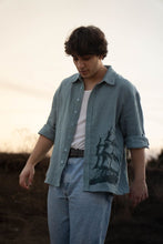 Load image into Gallery viewer, Man wearing a light blue shirt with a graphic design outdoors

