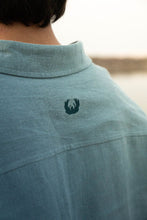 Load image into Gallery viewer, Close-up of a light blue shirt with a logo on the back.
